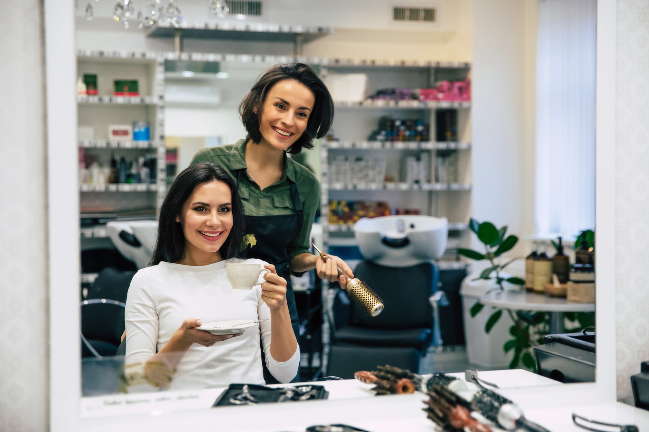 peluquera profecional sonriendo al espejo junto a su cliente scaled
